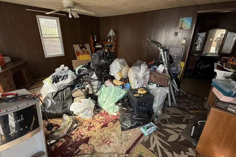 Wood-paneled room piled with trash bags, boxes and household items