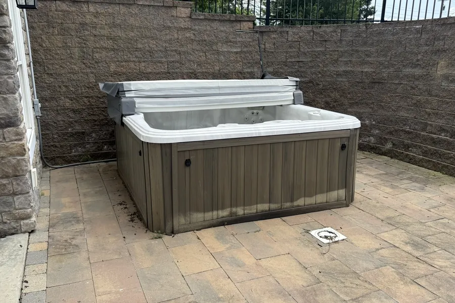 Hot tub sitting on a paver patio against a stone retaining wall, before removal