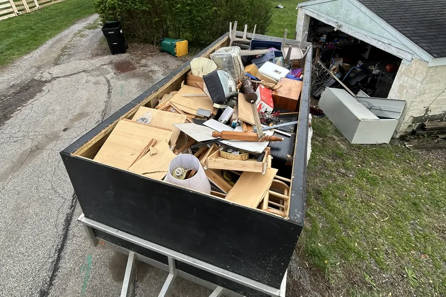 Trailer loaded with furniture, boards and household junk beside a garage
