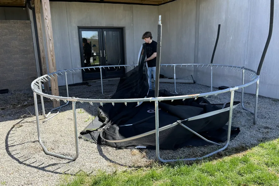 Worker taking apart a trampoline frame on a gravel patio under a deck